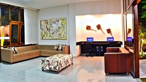 A modern living room with a sectional sofa, a patterned ottoman, and a desk with two laptops. - Atlantida Park Hotel (Porto Seguro)