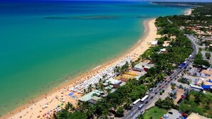 An aerial view of a beach with a road running parallel to the shore, lined with beach umbrellas and a few buildings.