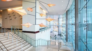 A modern hotel lobby with a glass staircase, metal railings, and hanging paper lanterns.
