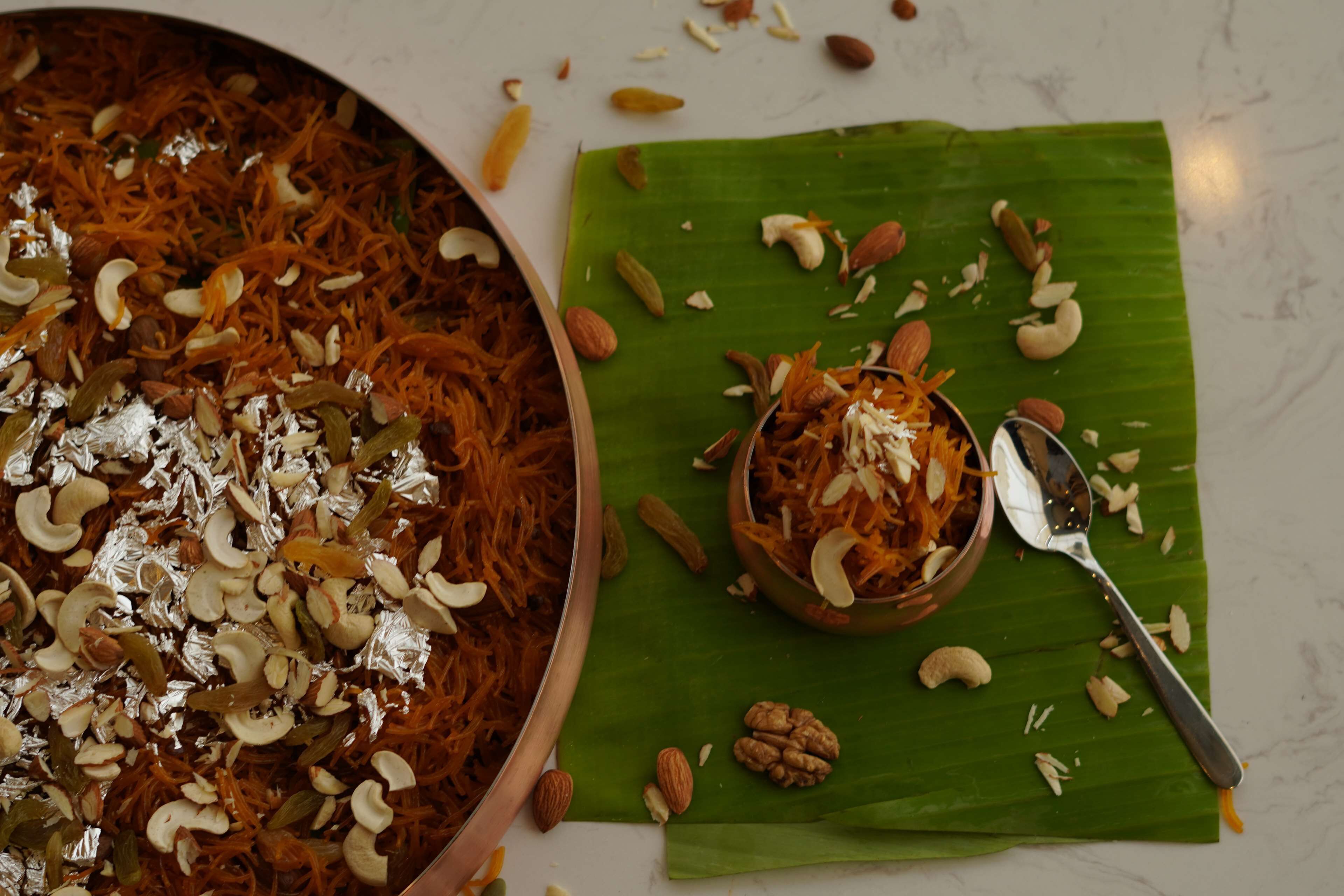 A large bowl of food with nuts and a spoon on a green leaf.