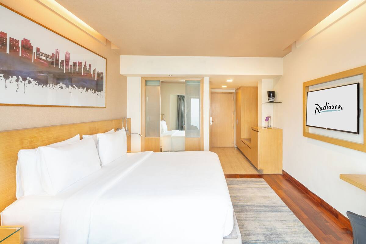 Quarto de hotel com uma cama grande, uma obra de arte com paisagem urbana, televisão e piso de madeira.