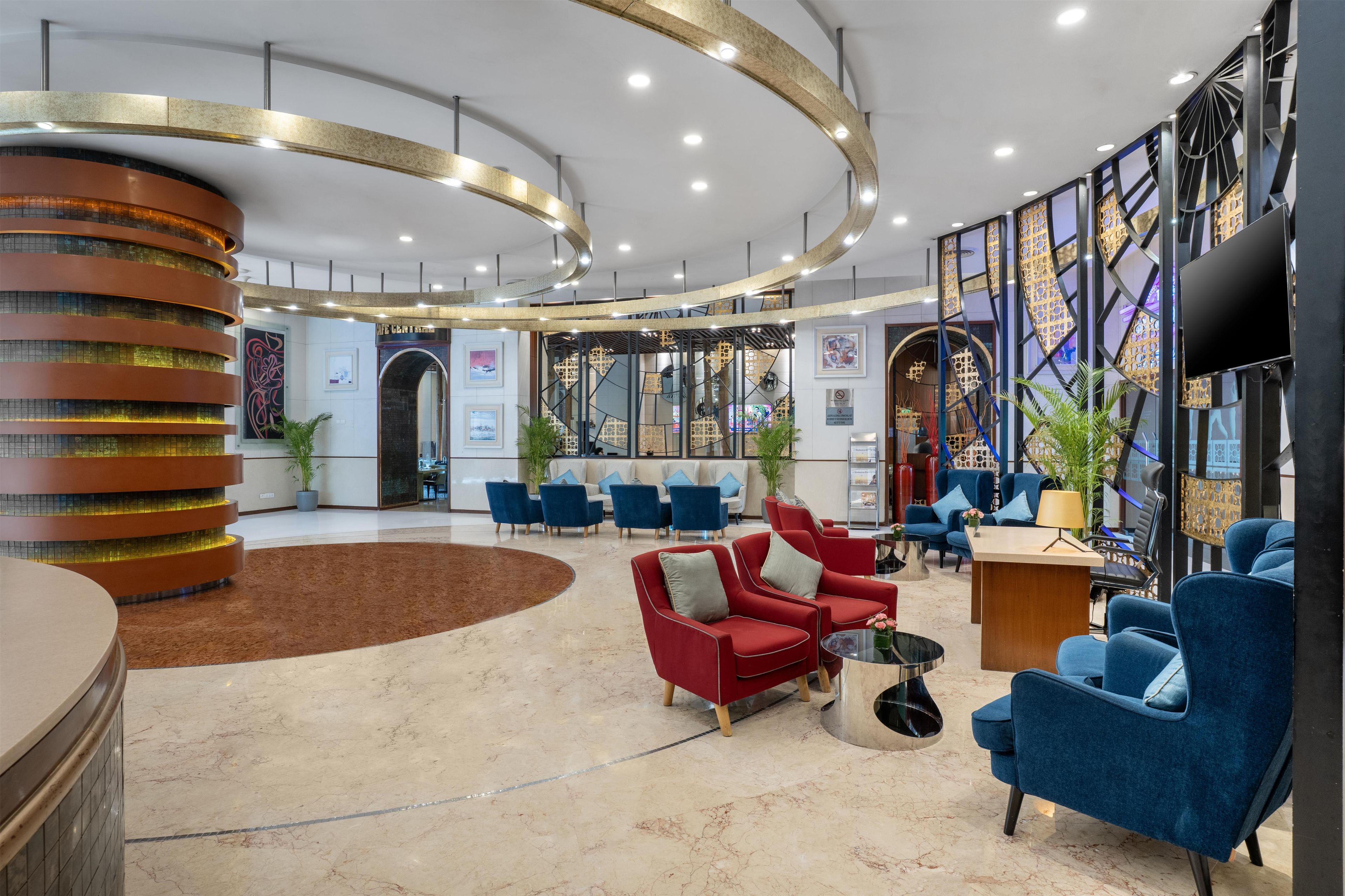 A modern lobby with a curved reception desk, seating area with red and blue chairs, and a large wall with decorative panels.