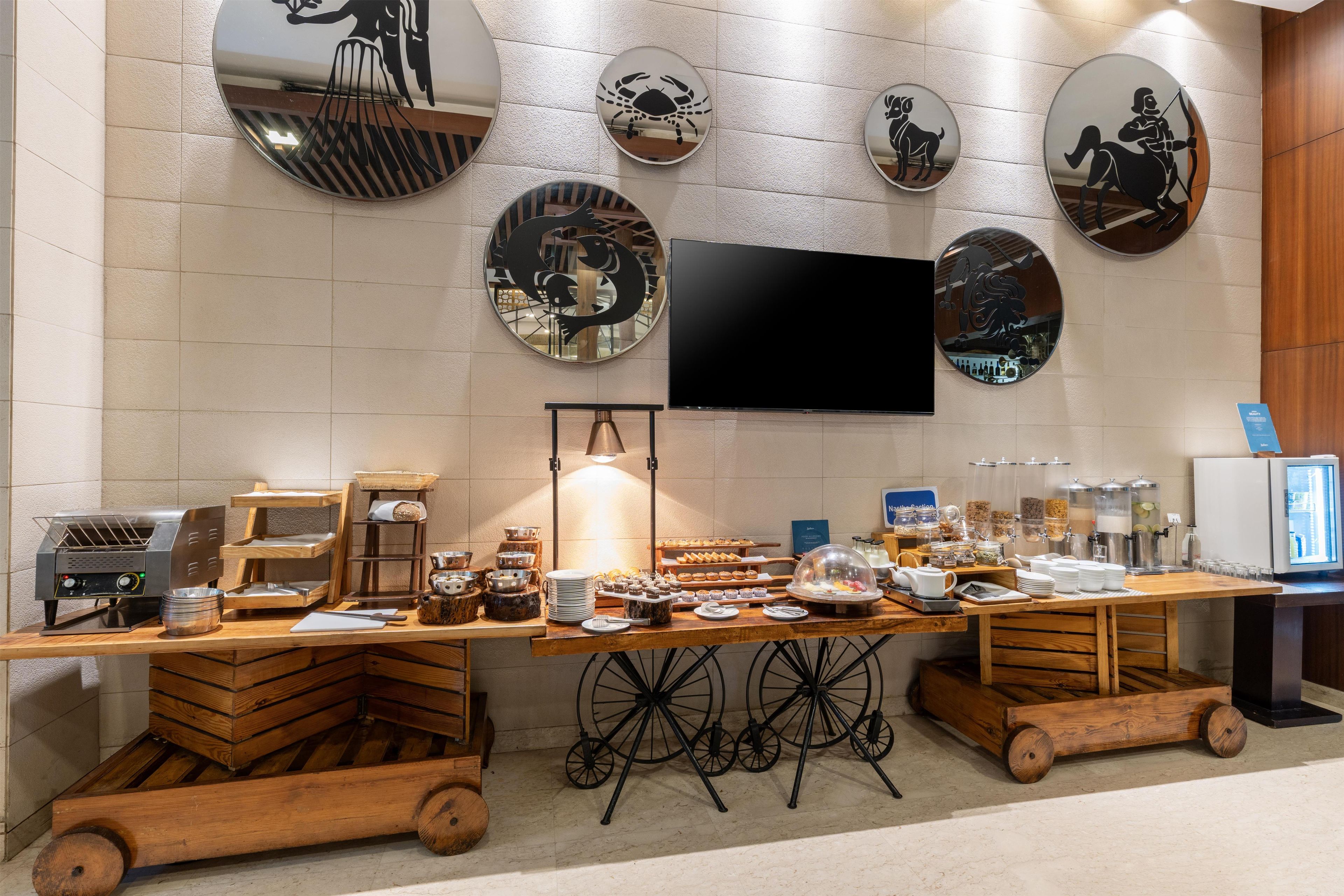 A breakfast buffet setup with a flat-screen TV mounted on the wall, surrounded by decorative wall mirrors.