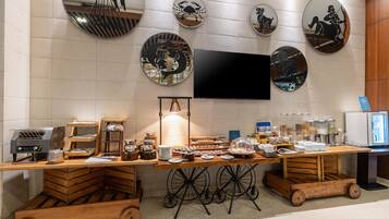 A breakfast buffet setup with a flat-screen TV mounted on the wall, surrounded by decorative wall mirrors.