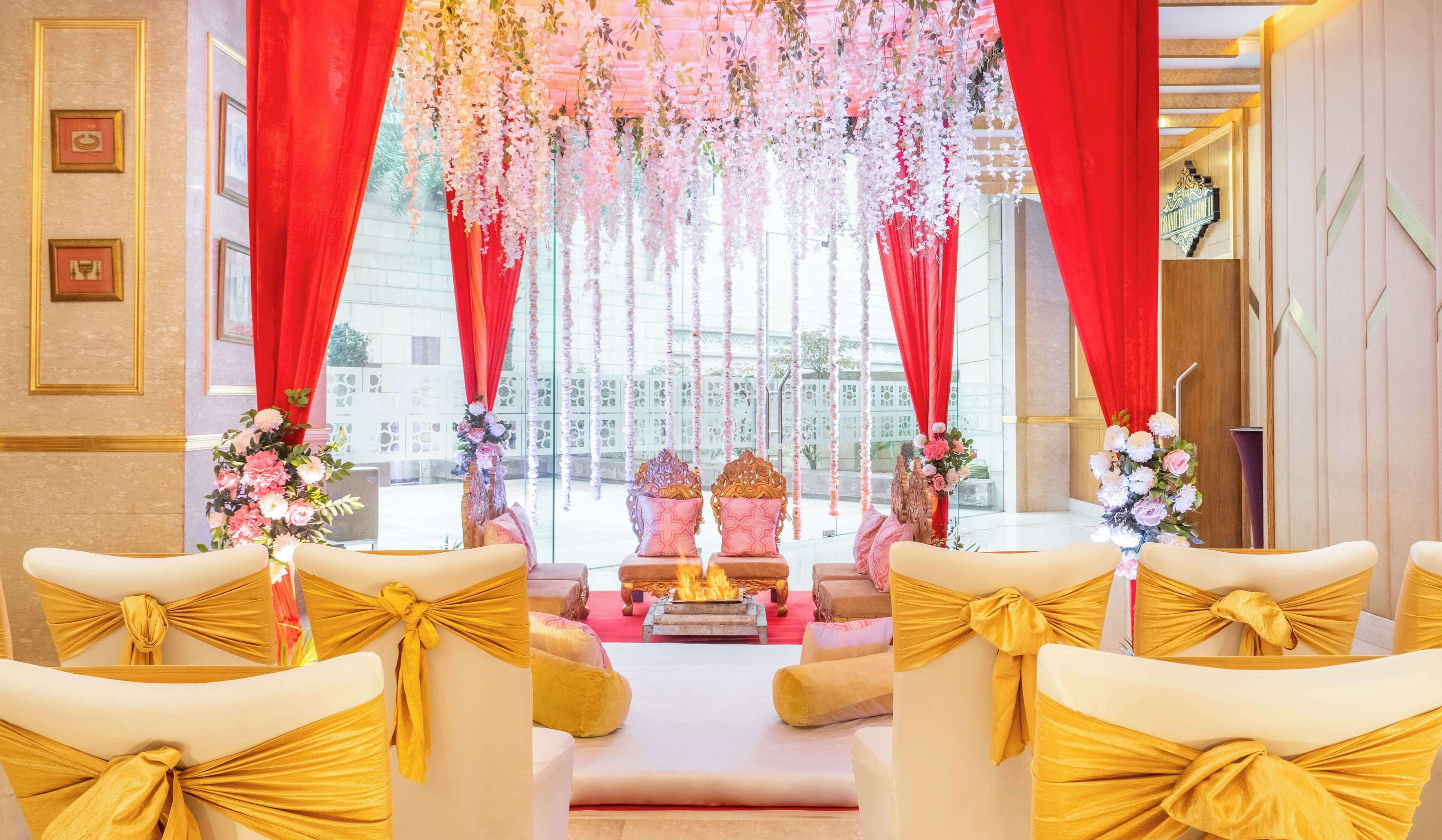 A wedding ceremony setup with a central altar, red curtains, and floral decorations.