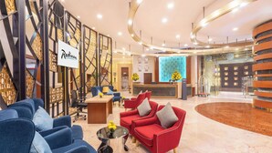 Een moderne lobby met een receptiebalie, blauwe en rode zitplaatsen en een decoratieve wand.