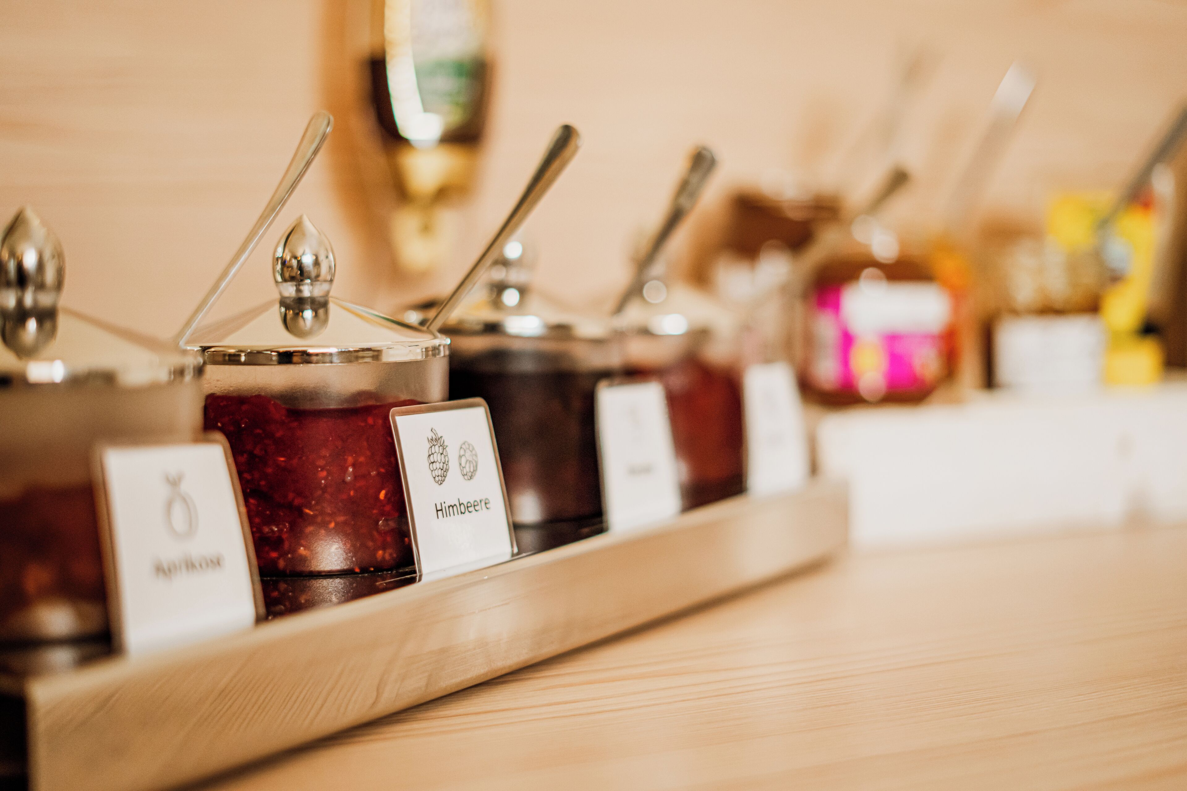 Una bandeja de madera con frascos de miel, incluyendo etiquetas con la leyenda 'Himbeere' y 'Kahkose'.