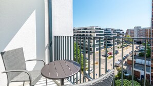 A balcony with a wicker chair and a small table, overlooking a parking lot and buildings. - Hotel an der Stadthalle Rostock-Hbf (Rostock)