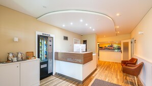 A reception area with a 'WELCOME' sign, a refrigerator, a coffee station, and a view of a cityscape through a window. - Hotel an der Stadthalle Rostock-Hbf (Rostock)