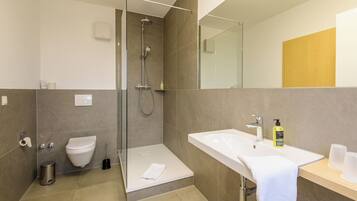Un baño moderno con ducha de vidrio, lavamanos blanco y un inodoro.
