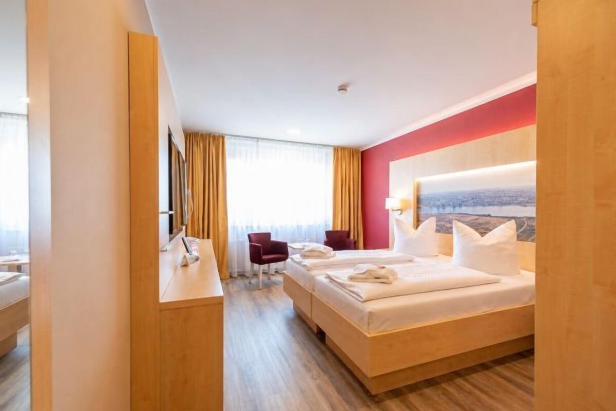 A hotel room with a bed, a desk, a chair, and a view of the city.