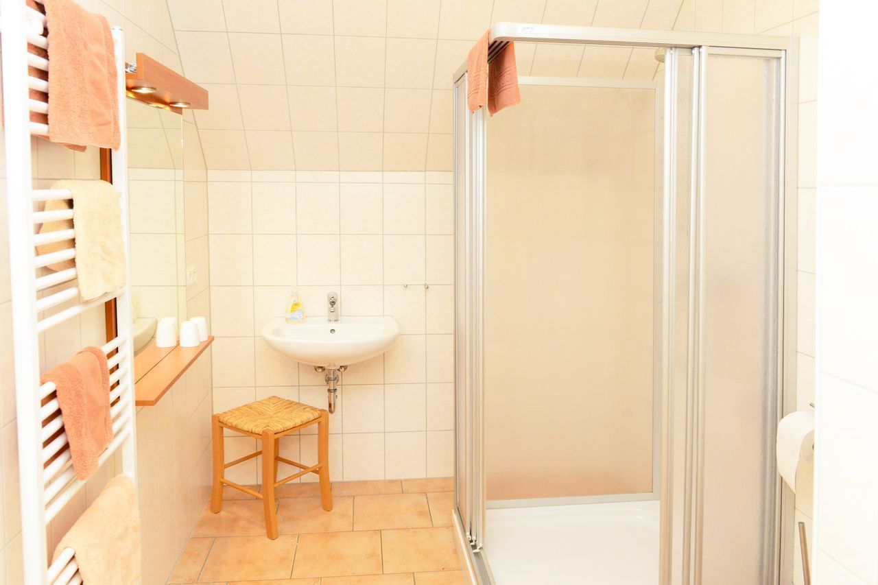 A bathroom with a white sink, a mirror, a towel rack, a wooden stool, and a glass shower enclosure.