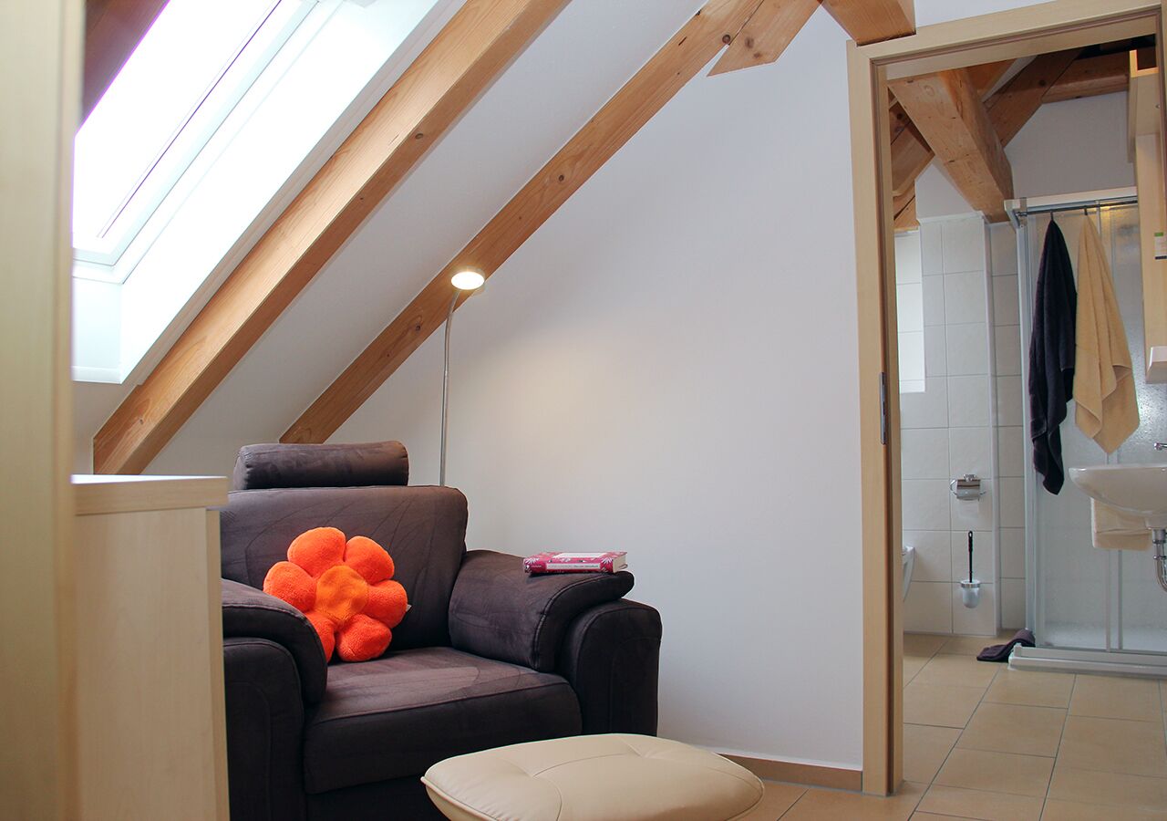 A cozy room with a sloped ceiling, a cushioned seating area, a small table, and a shower area.