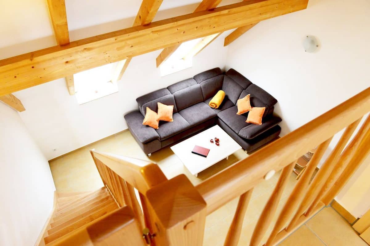 Um quarto moderno no estilo loft, com um sofá seccional cinza escuro, vigas de madeira, uma mesa de centro branca e uma escada.