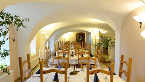A long dining table with chairs, candles, and table settings in a room with arched ceilings and a plant.