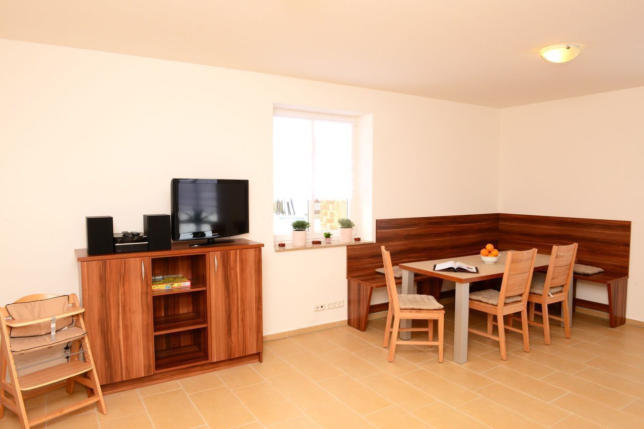 A compact living space with a wooden cabinet, a television, a dining table with chairs, and a small window with plants.