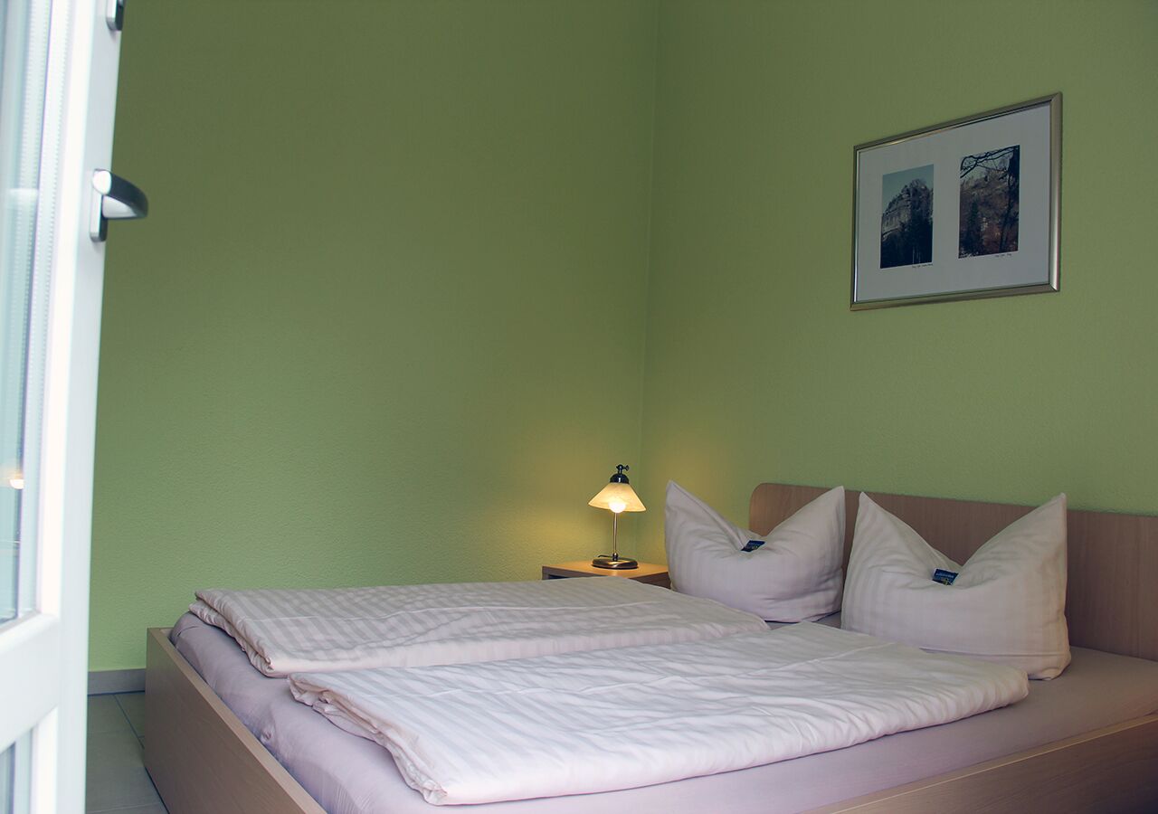 Una cama bien tendida con un almohadón y una lámpara de noche en una habitación con paredes verdes.