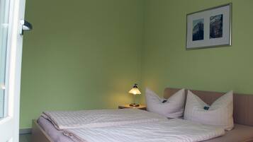 Una cama bien tendida con un almohadón y una lámpara de noche en una habitación con paredes verdes.