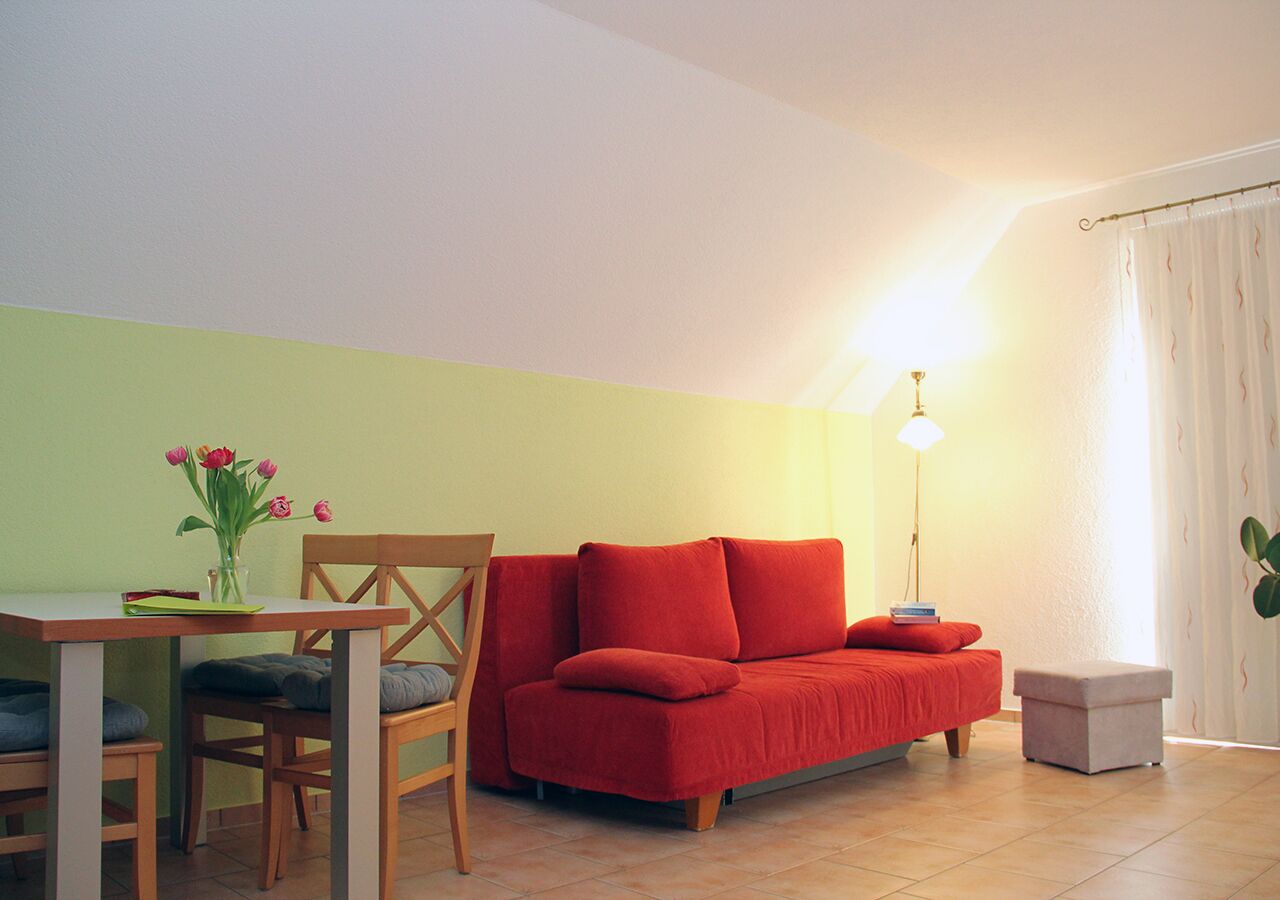 Una habitación con un sofá rojo, una silla de madera, una mesita con un jarrón de flores y una lámpara de pie.