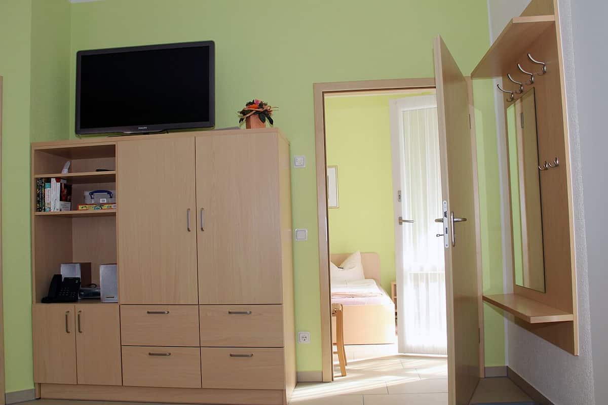 Quarto com cama, guarda-roupa, televisão e porta que dá para outro espaço.