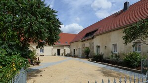 A courtyard with a paved walkway, a metal fence, and a building with a red-tiled roof.