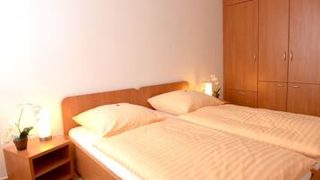A double bed with two pillows, a nightstand with a lamp and a potted plant, and a wooden wardrobe.