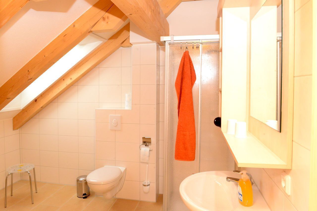 A small bathroom with a toilet, sink, and shower. There is a wooden beam ceiling and a towel hanging on the shower door.