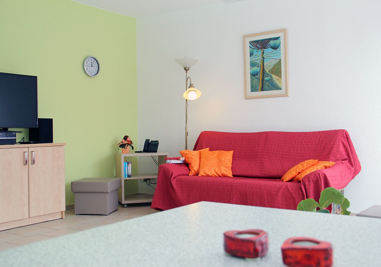 En stue med en rød sofa, et lille bord, en lampe, et ur og et billede på væggen.