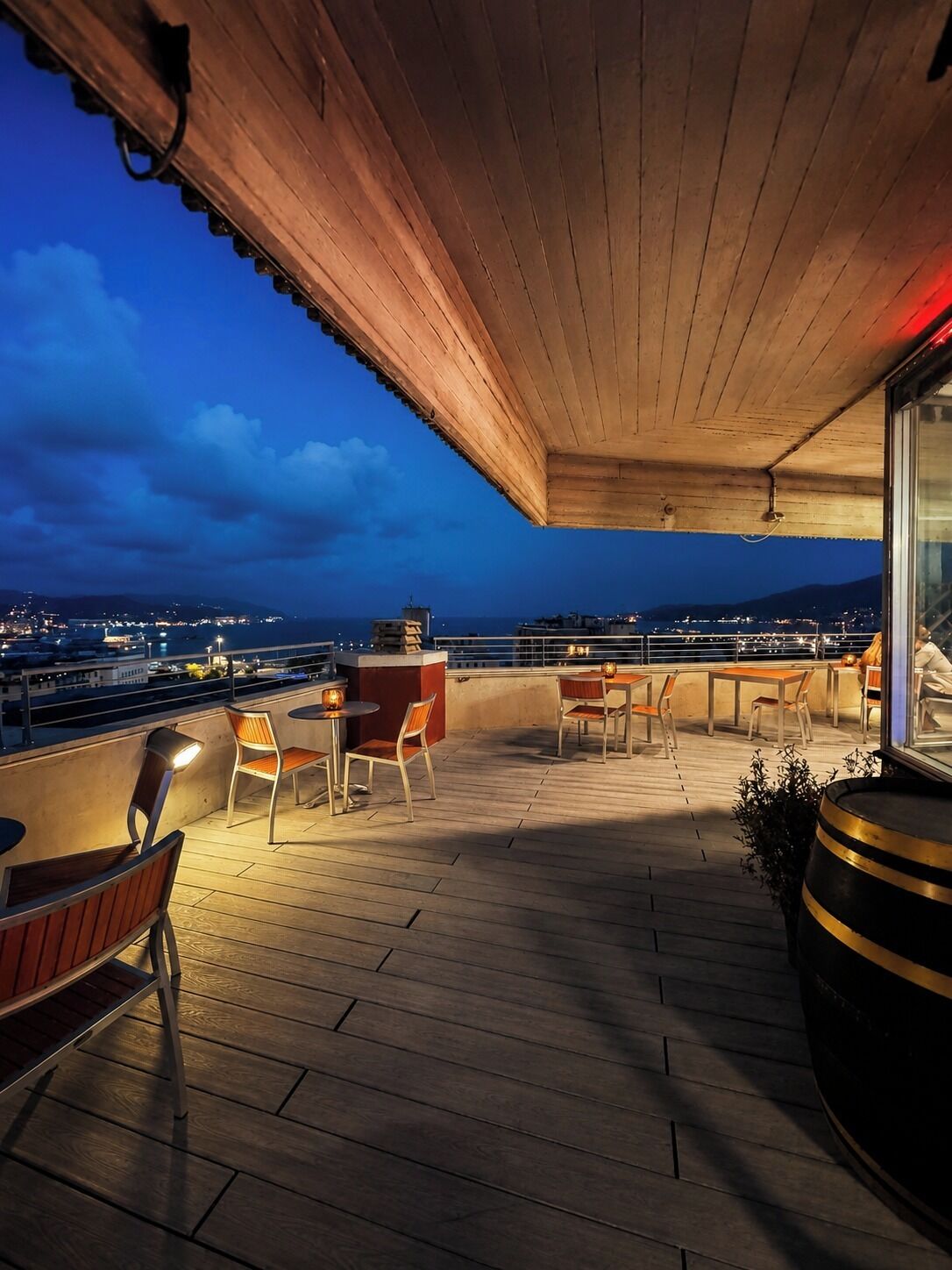 Terraza de madera con mobiliario exterior y vistas a la ciudad al atardecer.