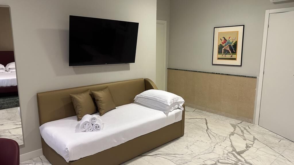 A hotel room with a bed, a flat-screen TV mounted on the wall, a framed picture on the wall, and a marble floor.