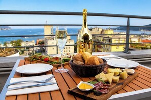 A table set with a bottle of champagne, a glass, plates, bread, cheese, and a charcuterie board with olives and a small bowl of sauce.