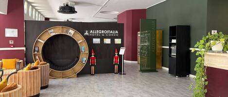 A modern hotel lobby with a circular seating area, a reception desk, and a sign for Allegroitalia Hotel & Condo.