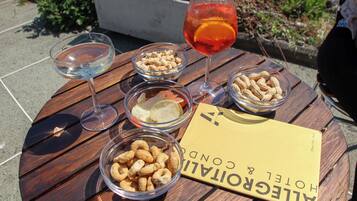 A wooden table with a glass of red drink, two glasses of white wine, and bowls of snacks. A yellow booklet titled "HOTEL & CONDO" is also visible.