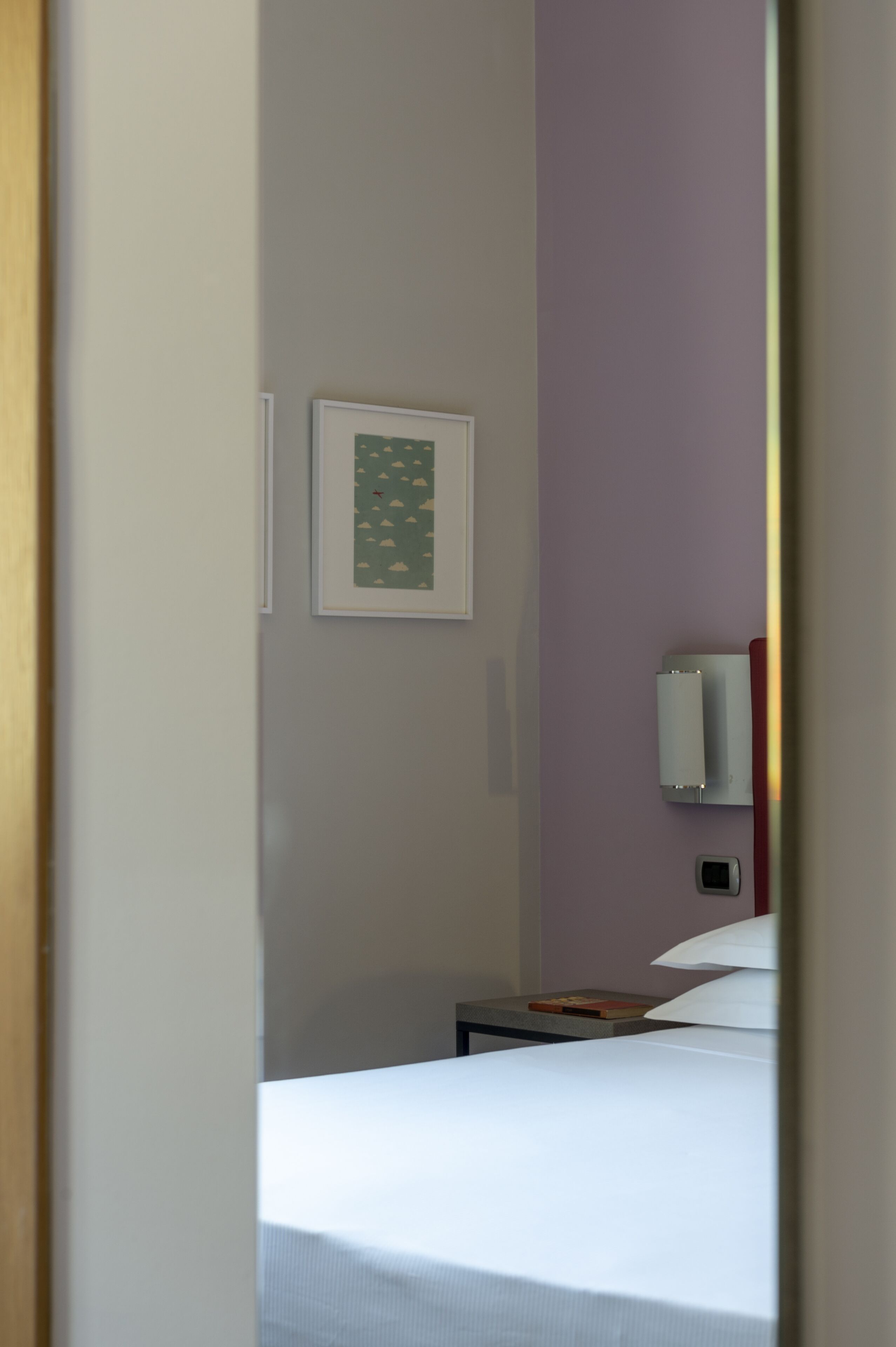 A hotel room with a bed, a nightstand, a framed picture, and a wall-mounted light fixture.