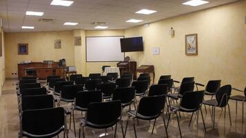 A conference room with rows of black chairs, a podium, a projector screen, and a television on the wall.