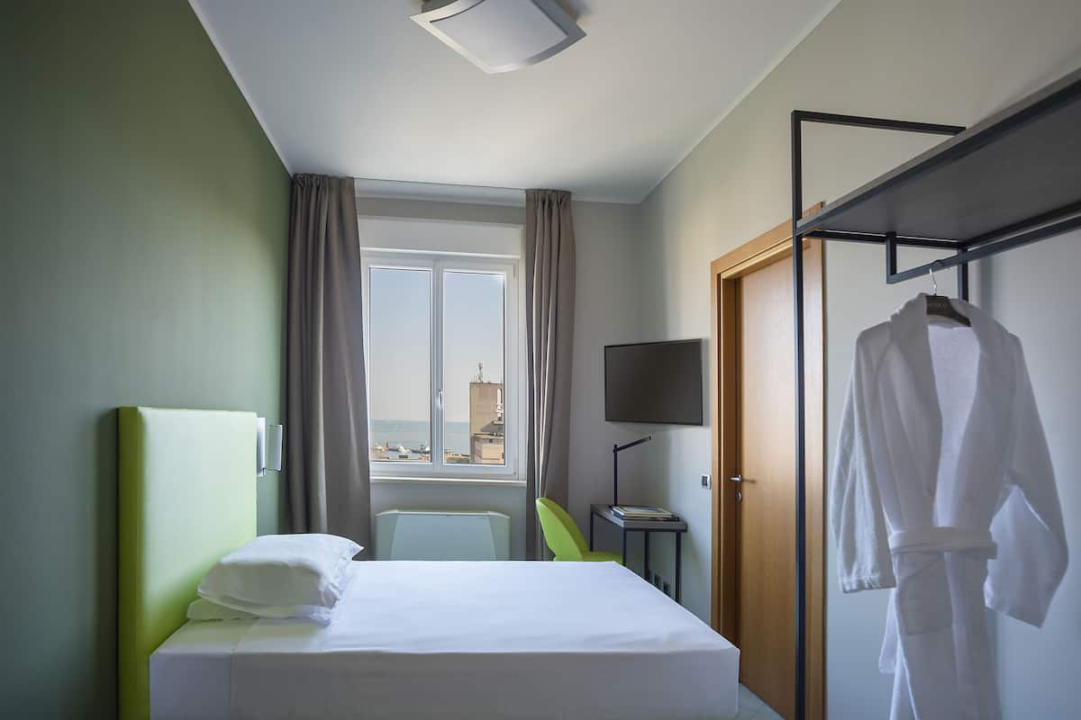 Habitación de hotel con cama, una silla, un televisor y una bata colgada en un perchero.