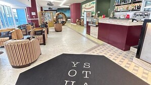 Un vestíbulo de hotel con mostrador de recepción, zona de estar y un letrero en el suelo que dice 'STAY YOUR'.