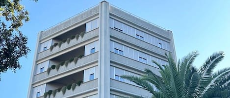 Un edificio de varios pisos con balcones, una palmera y una cerca.