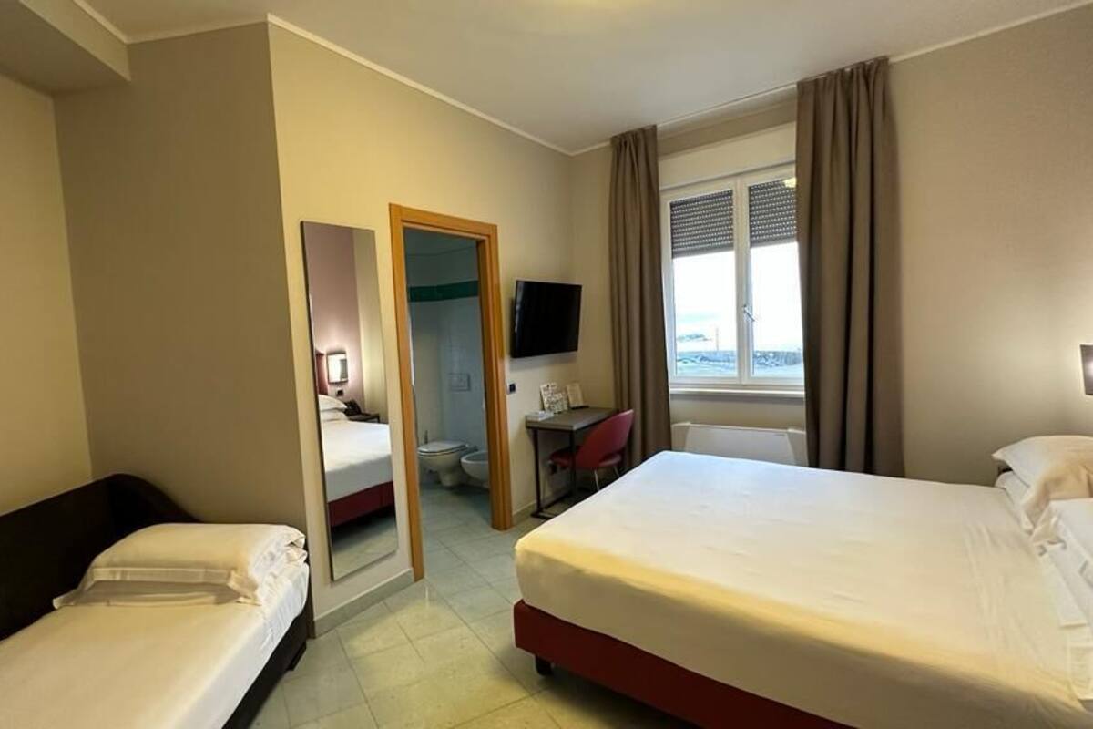 Habitación de hotel con dos camas, un escritorio, una silla, un televisor y un baño visible a través de una puerta abierta.