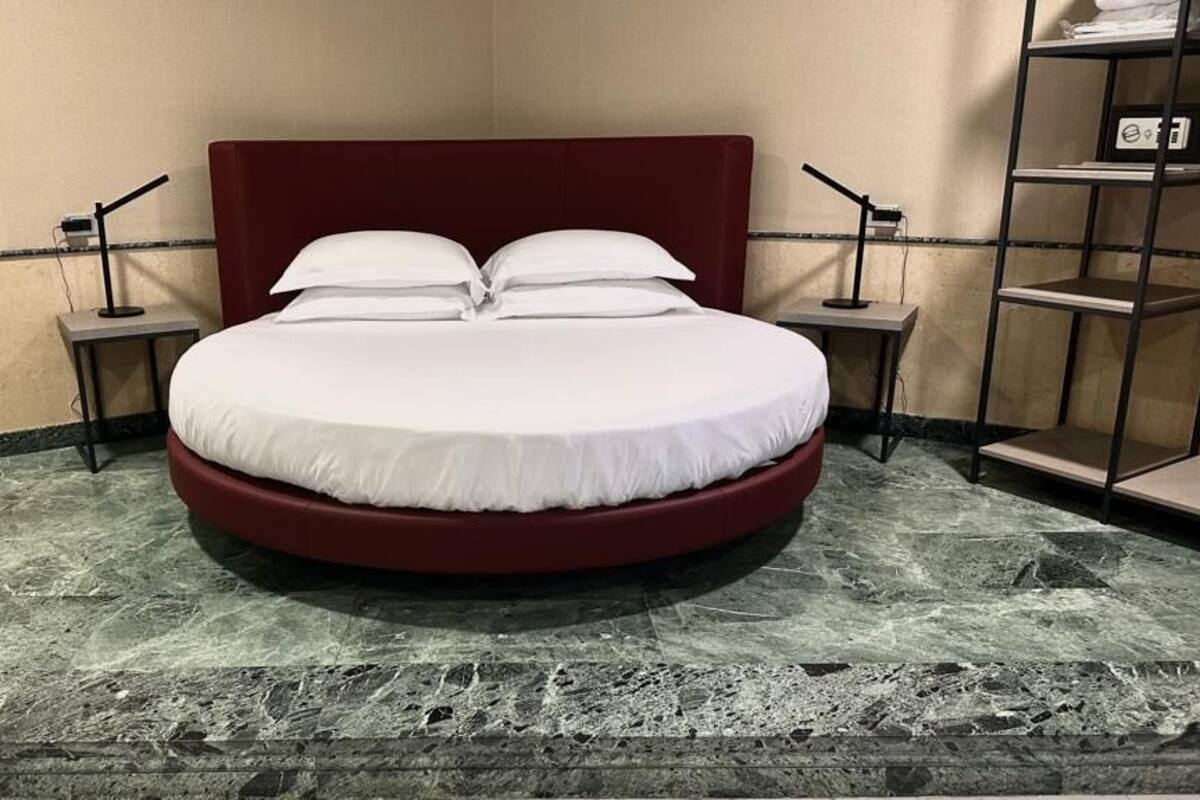 Una cama con cabecera roja en una habitación con piso de mármol y dos mesitas de noche con lámparas.