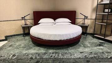 Una cama con cabecera roja en una habitación con piso de mármol y dos mesitas de noche con lámparas.