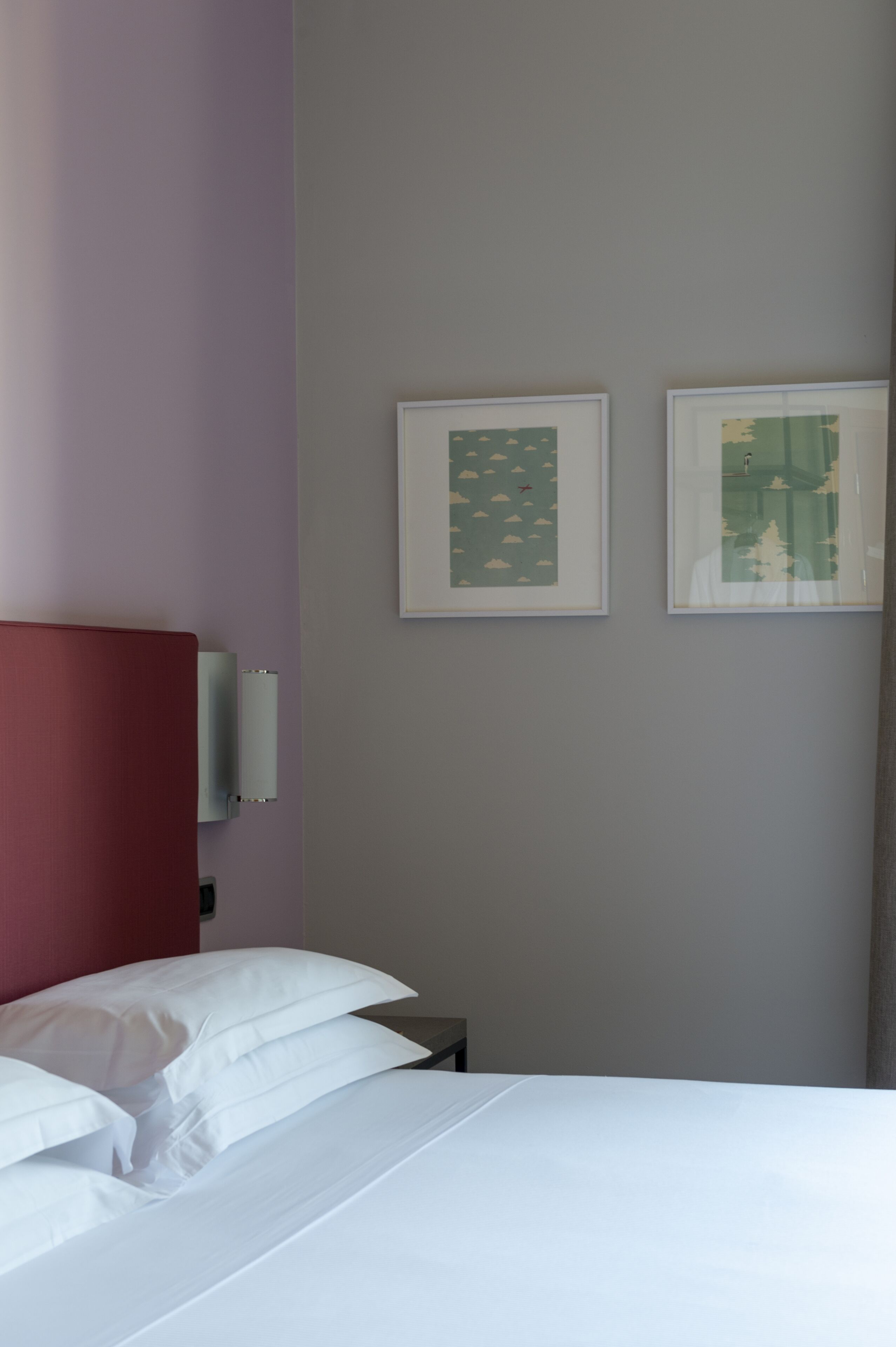 Una habitación de hotel con una cama, un cabecero rojo y dos cuadros en la pared.