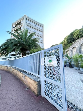 A gated entrance with a sign indicating a reception area, a palm tree, and a building in the background.