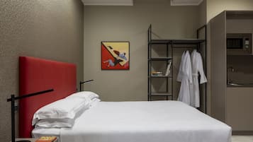 Quarto de hotel com cabeceira vermelha, roupa de cama branca, um quadro na parede, uma estante de livros e um guarda-roupa.