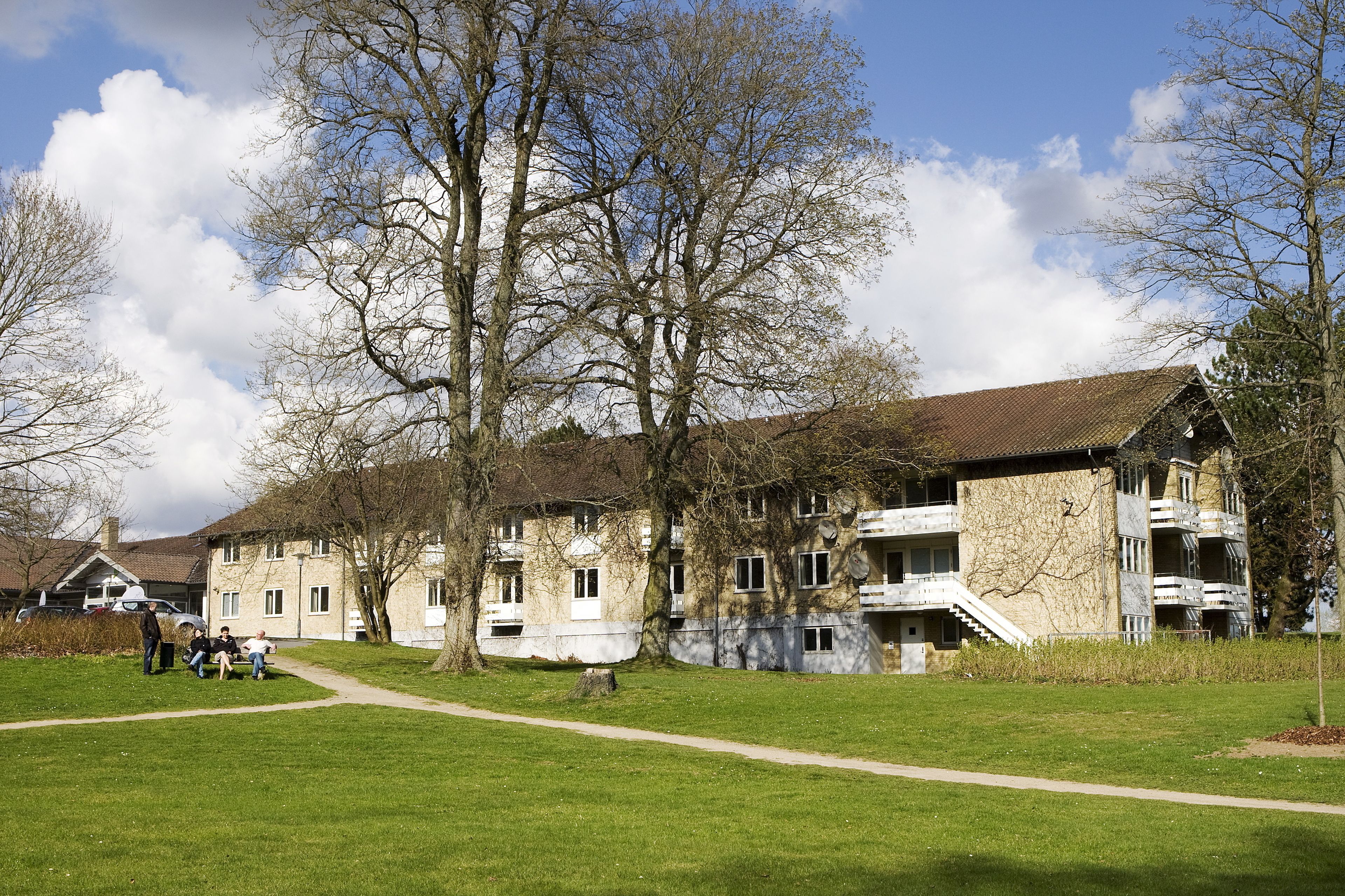 A building with multiple balconies, a paved pathway, and a grassy area.