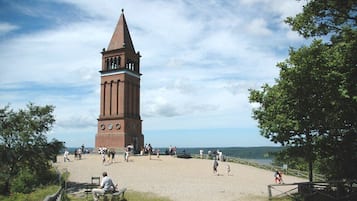A brick clock tower with a pointed roof, surrounded by a gravel area with people walking and sitting.