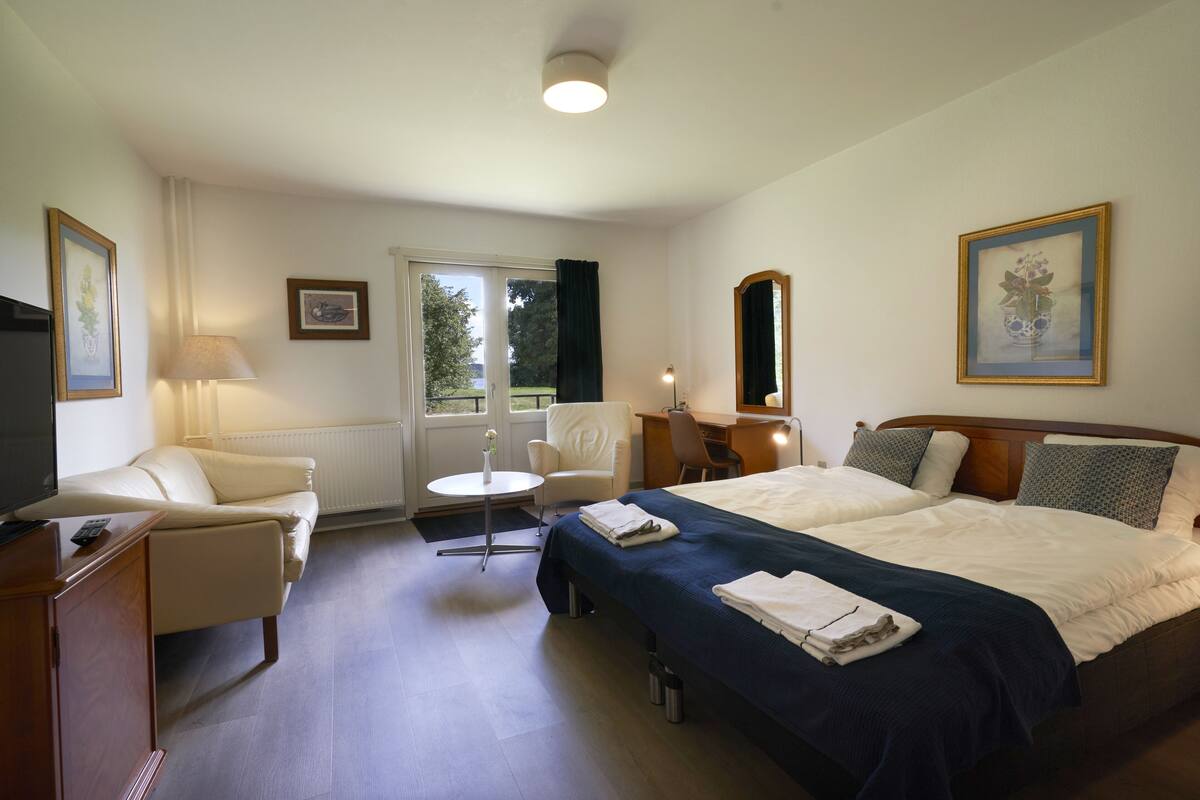 A hotel room with a bed, a desk, a chair, a TV, and a window with curtains.