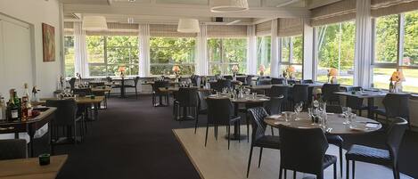 Un restaurante espacioso con varias mesas y sillas, amplias ventanas que ofrecen vistas al exterior y una decoración interior moderna y elegante.