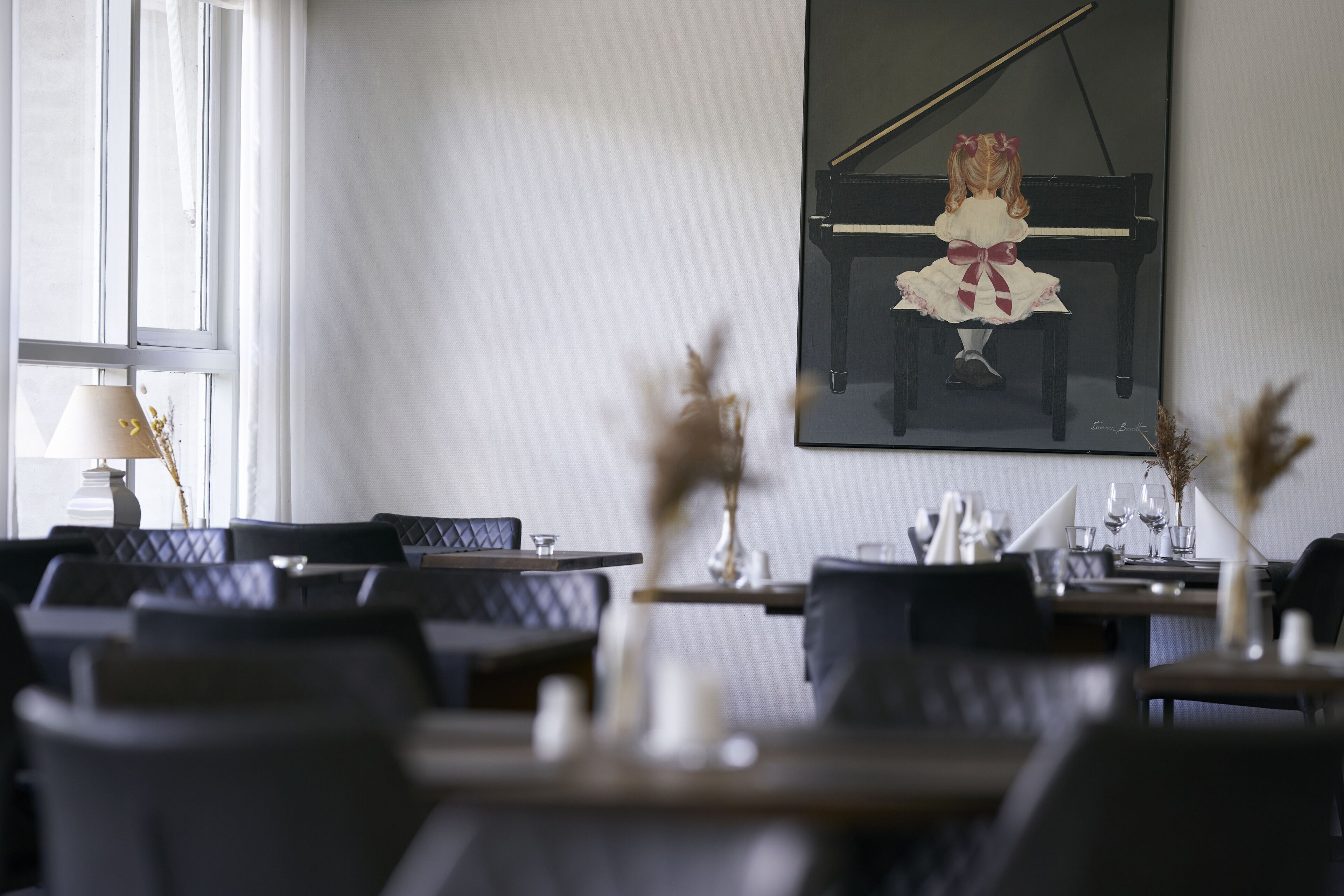 En matplats med bord för två personer, ett piano och ett fönster med gardiner.