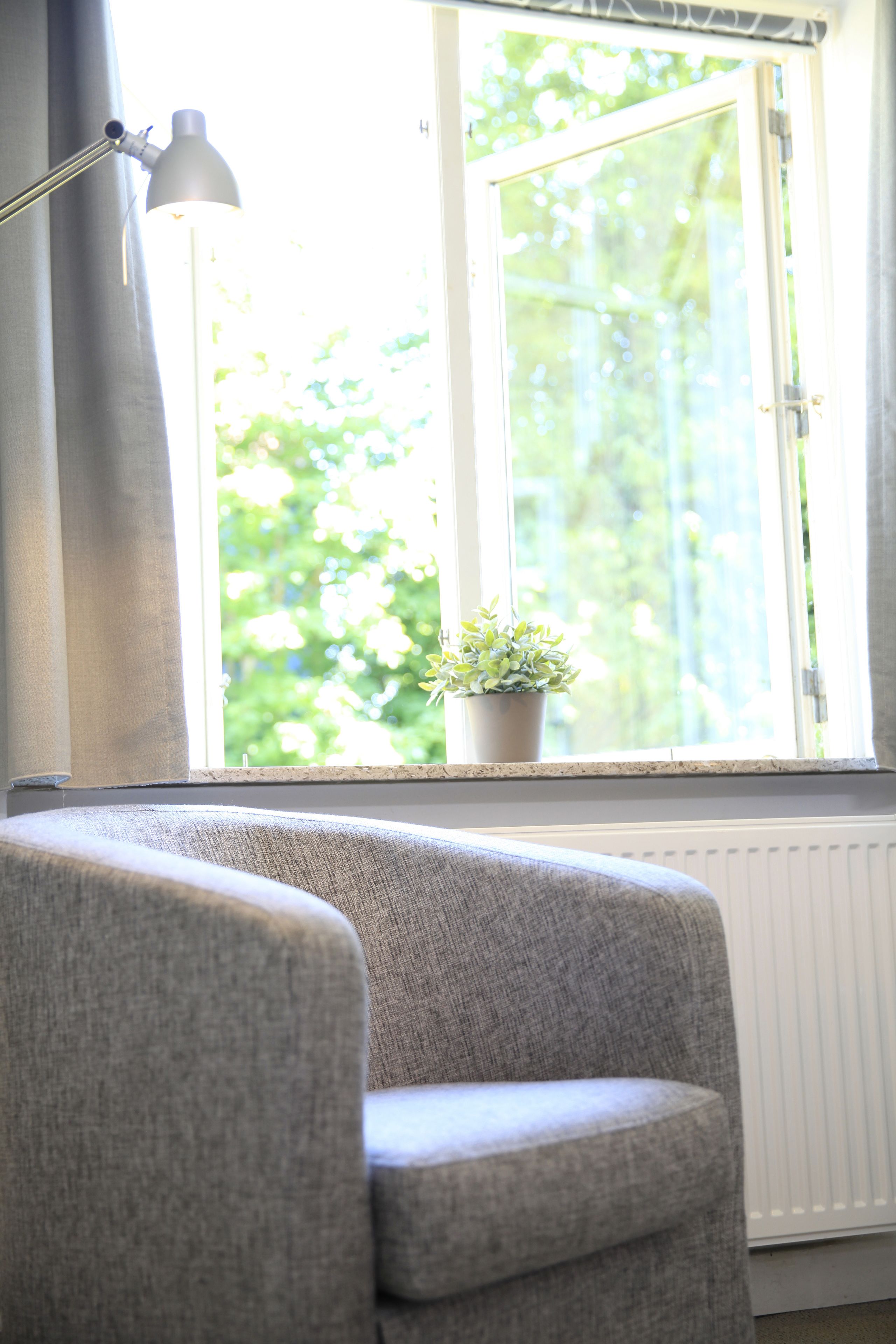 Et værelse med et vindue, en radiator, en grå lænestol og en gulvlampe.